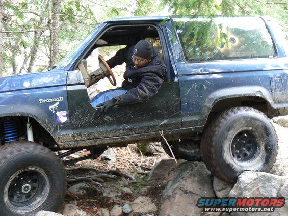 Driver in a blue 1986 Ford Bronco II navigating rocks on a trail
