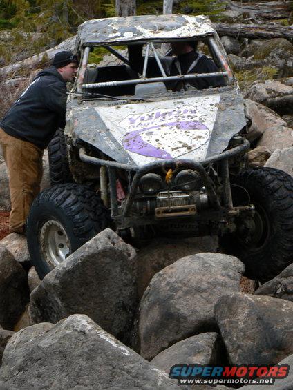 Mud-covered off-road vehicle with purple graphics navigating large rocks