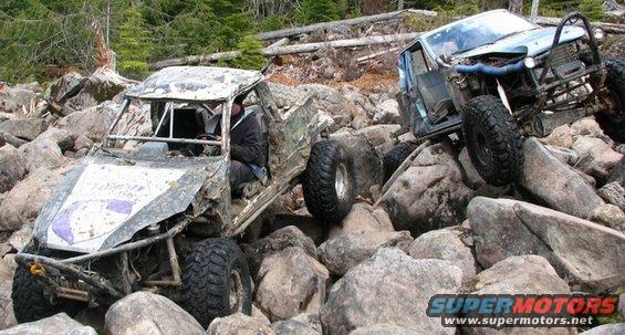 Two heavily modified off-road vehicles are stuck on a large rock obstacle course