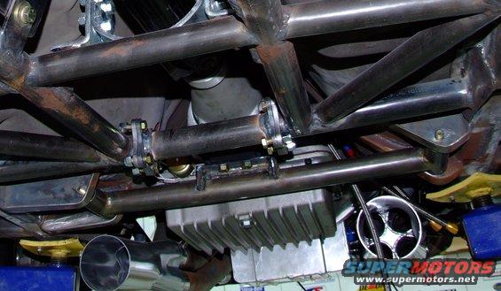 Underside view of a vehicle with a custom roll cage, exhaust pipes, and a large oil pan