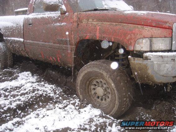 Mud-covered red pickup truck with snow on the ground, stuck in mud