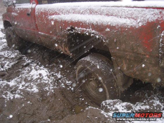 red pickup truck stuck in mud and snow, rear wheel deep in mud