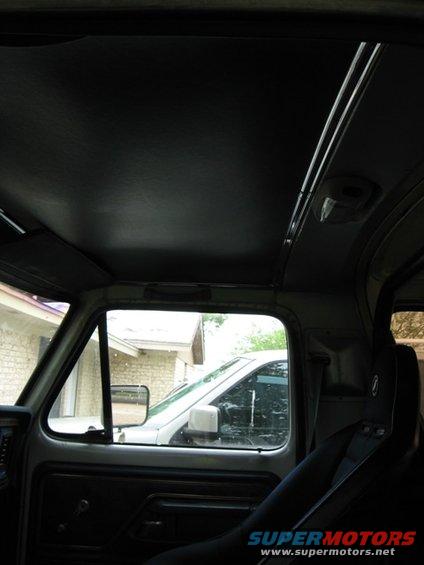 Inside a truck, looking out the passenger window at another truck. The interior has a black headliner and door panel