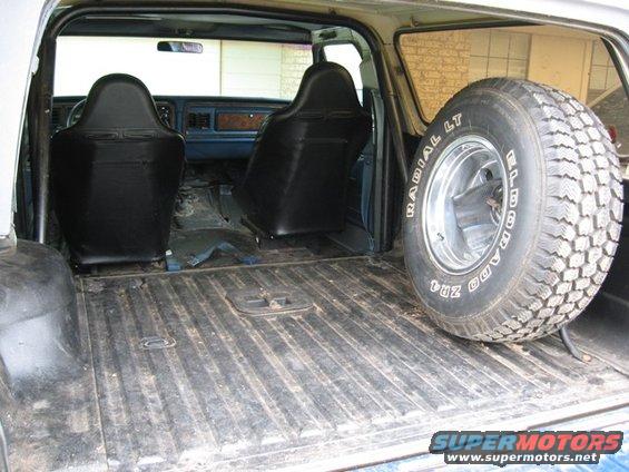 Interior view of a vehicle showing two black bucket seats and a spare tire on the right