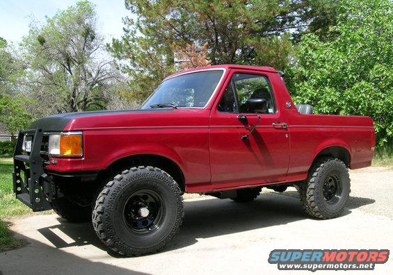 1991 Ford Bronco, red, with black aftermarket front bumper and off-road tires