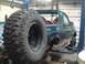 1996 Ford Bronco - Green Ford Bronco on a lift with a large spare tire, showing rust damage and missing body panels.