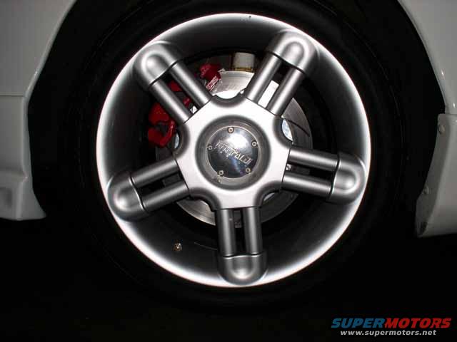 Close-up of a car's wheel with a unique five-spoke design and red brake caliper visible
