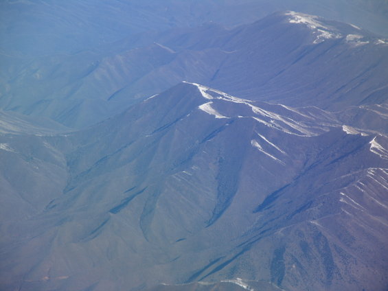 Aerial view of snow-dusted mountains under a hazy blue sky