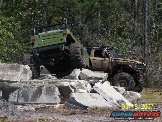 tan 1980s Ford Bronco and green Jeep Wrangler climbing over concrete blocks