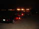 1989 Ford Taurus - A black sedan tows a trailer and a pickup truck in the dark.