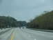 1995 Ford C-350 (Centurion Conversions) - A view from a vehicle traveling on a highway with trees and hills on the side.