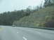 1995 Ford C-350 (Centurion Conversions) - Driving on a highway next to a large rock cut with trees and two vehicles visible.