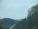 1995 Ford C-350 (Centurion Conversions) - A scenic view of a highway cutting through rolling hills and dense trees under a cloudy sky.