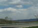 1995 Ford C-350 (Centurion Conversions) - A view of a rural landscape with rolling hills and a highway guardrail under a cloudy sky, taken from a vehicle.