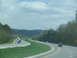 1995 Ford C-350 (Centurion Conversions) - Vehicles travel on a multi-lane highway surrounded by green hills and trees under a cloudy sky.