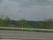 1995 Ford C-350 (Centurion Conversions) - A view of a highway guardrail and trees with distant hills under a cloudy sky.