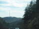 1995 Ford C-350 (Centurion Conversions) - A view from the road shows a cell tower on a wooded hill under a cloudy sky.