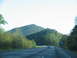 1995 Ford C-350 (Centurion Conversions) - A white van travels down a highway surrounded by trees and mountains under a clear sky.