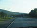 1995 Ford C-350 (Centurion Conversions) - View from a car driving on a highway with other vehicles and a wooded hillside.