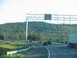 1995 Ford C-350 (Centurion Conversions) - Cars and a truck travel on a highway with wooded hills in the background.