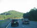 1995 Ford C-350 (Centurion Conversions) - Two vehicles travel down a highway with a large, green hill visible in the distance.