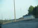1995 Ford C-350 (Centurion Conversions) - A distant city skyline is visible beyond a concrete barrier and trees under a clear sky.