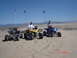1981 Ford Bronco - Three ATVs are parked on sand dunes under a clear blue sky, with riders seated and flags attached to poles.