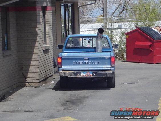 Blue Chevrolet pickup truck, rear view, with large exhaust pipe exiting bed, dirty bumper, license plate 946 UOZ