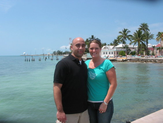 Couple standing on a pier with palm trees and buildings in the background