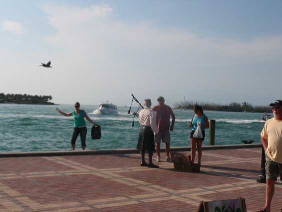 People on a brick pier with boats in the turquoise water under a hazy sky