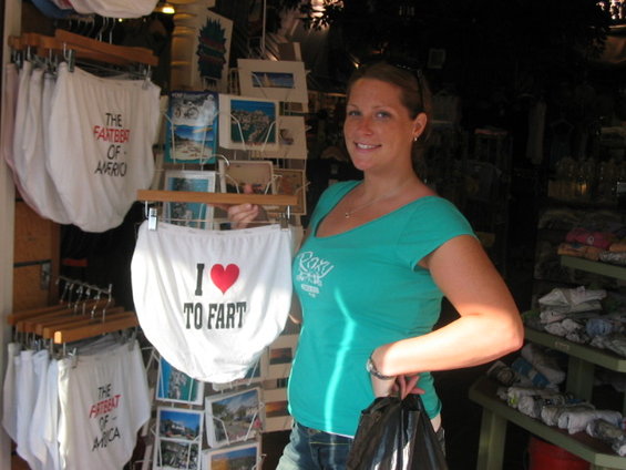 Woman holding up novelty underwear that says 'I ❤️ TO FART' in a shop with other novelty items for sale