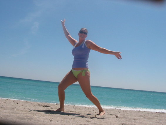 Woman in blue tank top and green bikini on sandy beach with ocean background