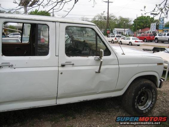 Side view of a white crew cab pickup truck, possibly from the 1980s. It has four doors and appears to be in used condition