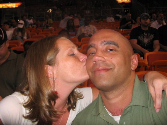 Woman kissing man's cheek in stadium seats, audience in background