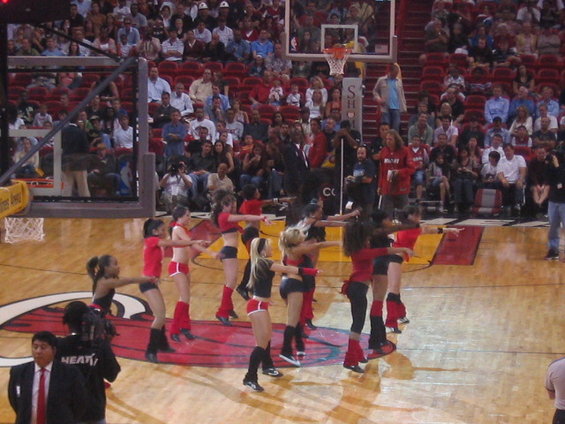 Cheerleaders in red and black outfits perform on a basketball court