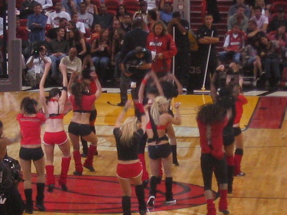 Cheerleaders in red and black outfits dance on a basketball court in front of a crowd