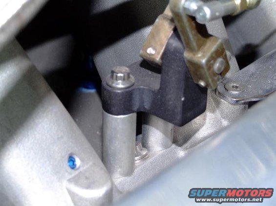 Close-up of a black bracket with a silver bolt and a brass lever attached to an engine component