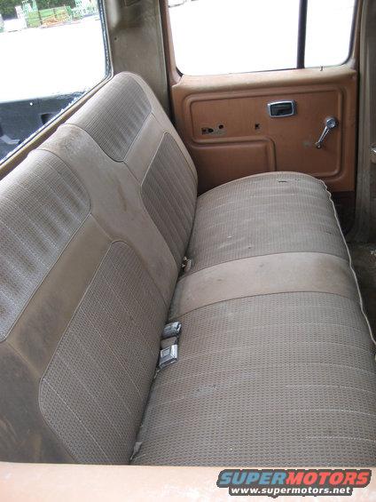 Interior shot of a worn bench seat in an older vehicle, showing fabric wear and a brown door panel