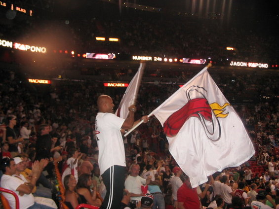 Man waves white flag with red and yellow logo in stadium crowd