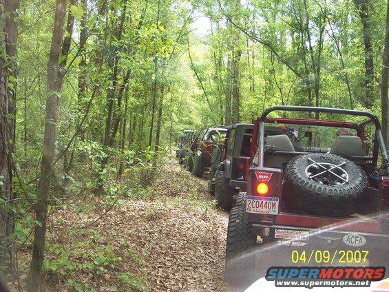 Red Jeep Wrangler with spare tire on rear, driving on a wooded trail