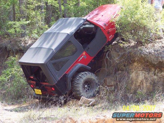 Red Jeep Wrangler tilted on its side on a dirt embankment with trees in the background