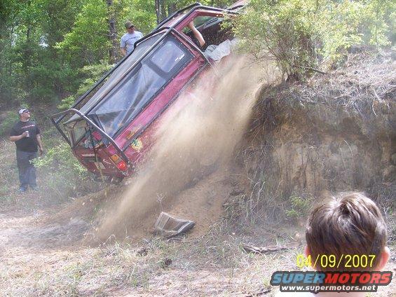 1984 Toyota 4Runner tilted on its side, stuck in mud on a dirt hill with people watching
