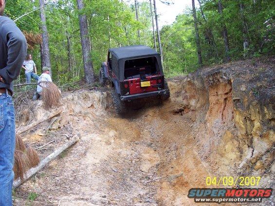 Jeep Wrangler going down a steep dirt trail with people watching