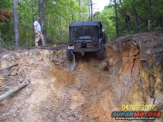Olive green Jeep Wrangler descending a steep dirt embankment, kicking up dust