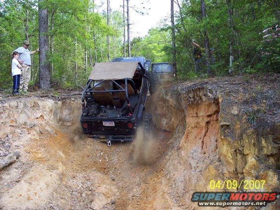 Off-road vehicle going down a steep dirt trail with another vehicle behind it. Two people watch from the top
