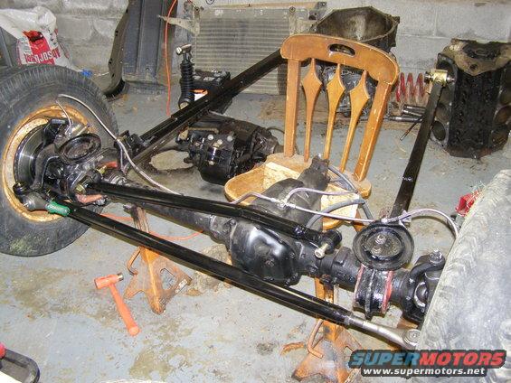 vehicle chassis with drivetrain components, transmission, and suspension parts on jack stands in a garage