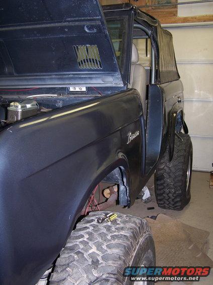 Dark blue Ford Bronco with hood open, showing off its front fender and large tires. The 'Bronco' script is visible on the side