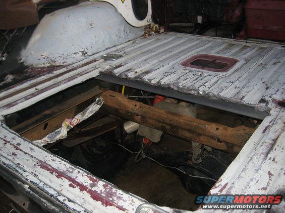 White vehicle bed with rusted metal floor, showing exposed frame and suspension components below