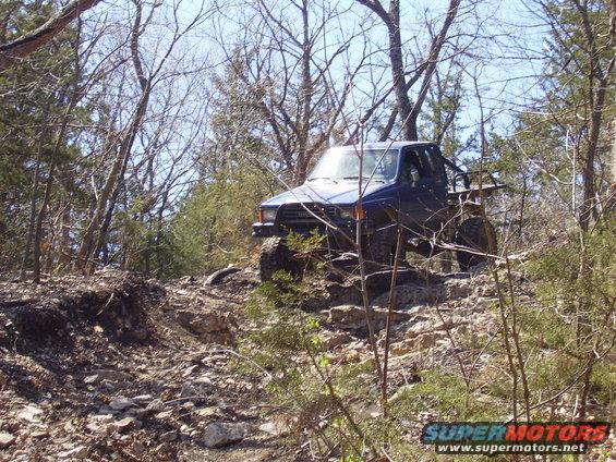 Blue pickup truck with off-road tires navigating a rocky incline