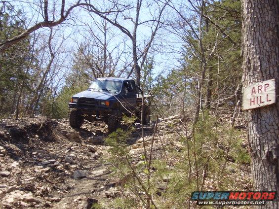 Blue pickup truck climbing a rocky hill, sign reads ARP HILL